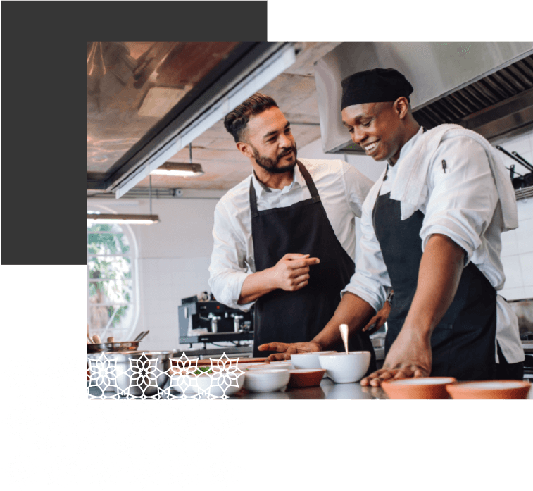 A couple of men standing in a kitchen preparing food.